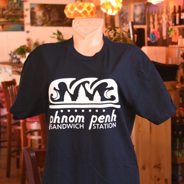 Dark blue Phnom Penh Sandwich Station t-shirt with white logo on a mannequin in a restaurant.