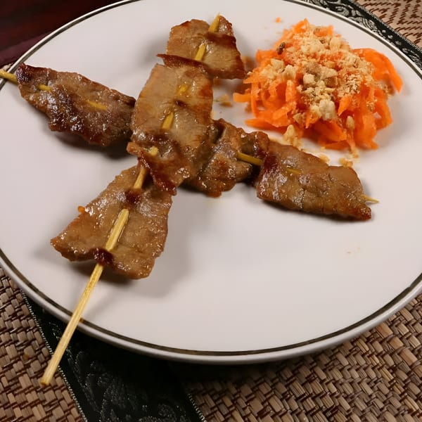 Cambodian beef skewers with shredded carrots and crushed peanuts on a white plate.
