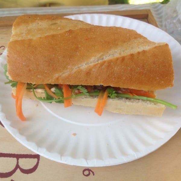 A Cambodian sandwich, or num pang, with carrots and cilantro on a white paper plate.