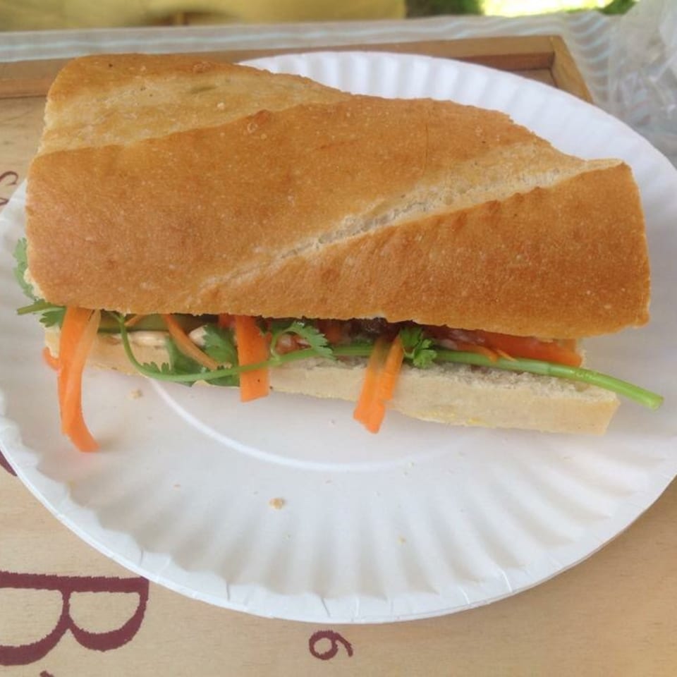 A Cambodian sandwich, or num pang, with carrots and cilantro on a white paper plate.