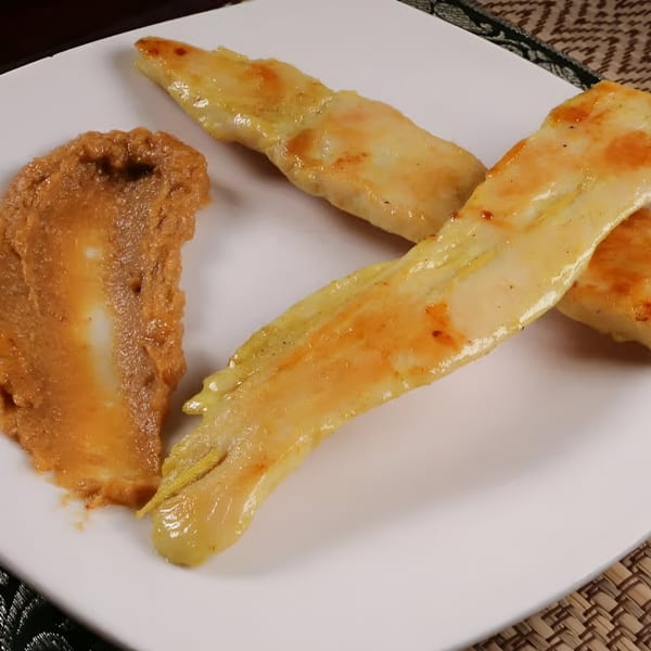 Three golden-brown chicken skewers with a dollop of peanut sauce on a white plate.