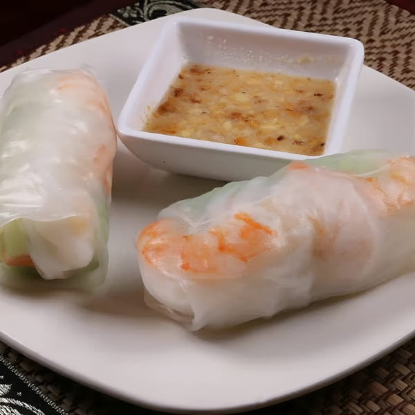 Two fresh shrimp spring rolls with a side of peanut dipping sauce on a white plate.